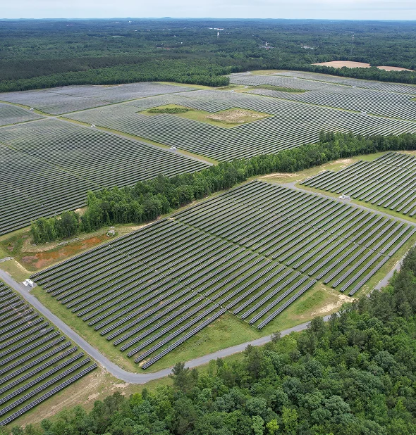 Aerial view of the Iona Energy project with rows of solar panels across a large rural site surrounded by forest.